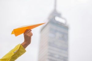 Hand holding an orange paper plane with the Torre Latinoamericana in the background, Mexico City.